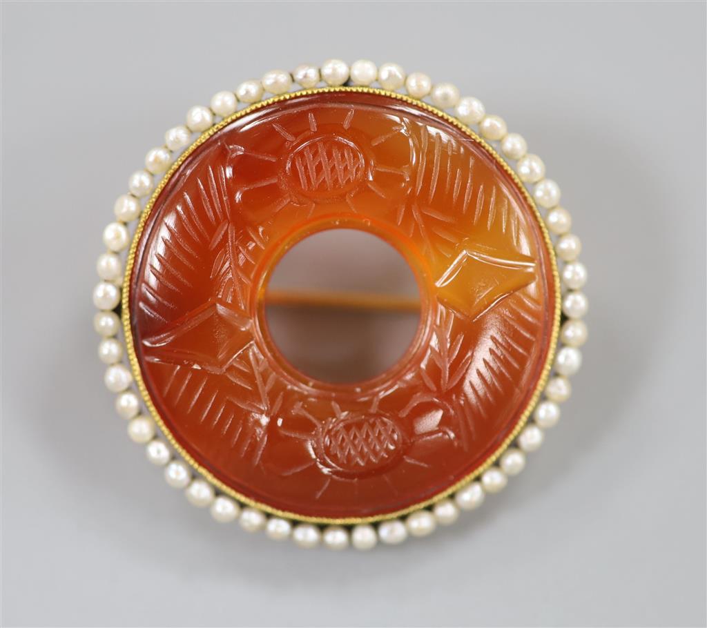 An early 20th century yellow metal(stamped 14), carved carnelian and seed pearl set openwork circular brooch, 27mm, gross 6.4 grams.